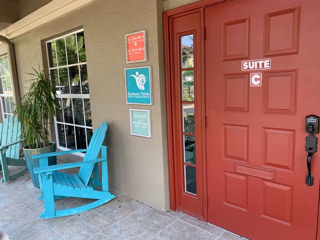 A red door labeled Suite C next to a window with a turquoise Adirondack chair outside. Signage on the wall includes information for Southwest Florida Lactation Services.